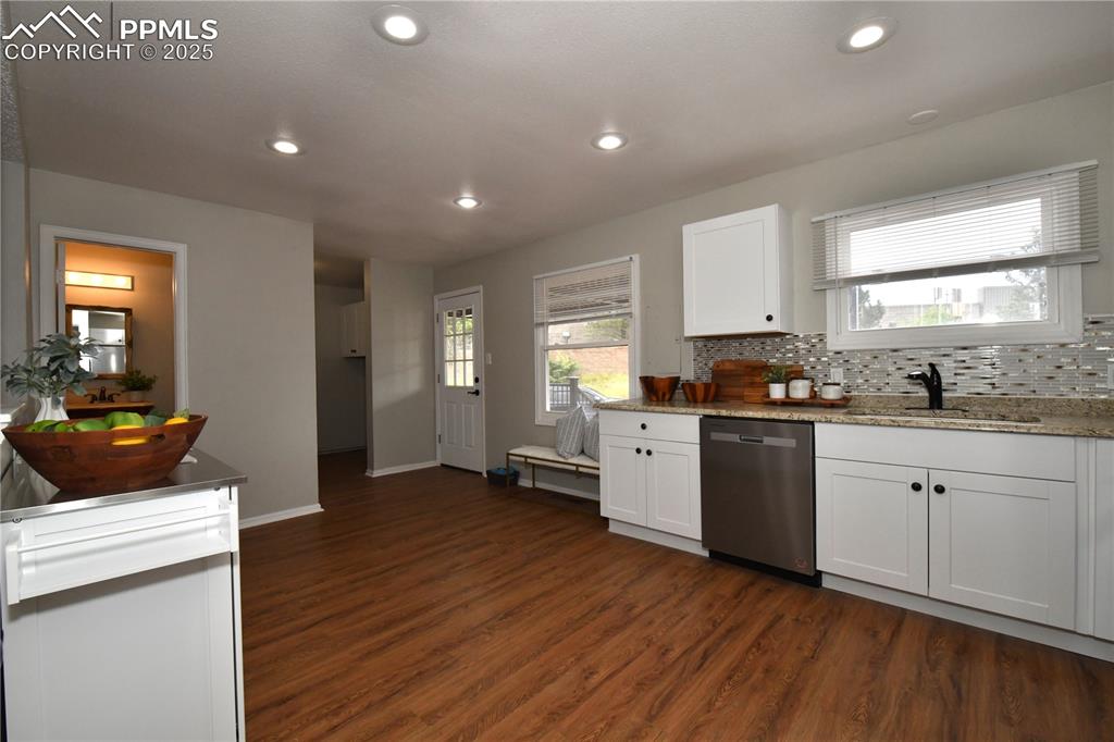 Image 14 of 36: Kitchen with backsplash, stainless steel dishwasher, white cabinets, dark w