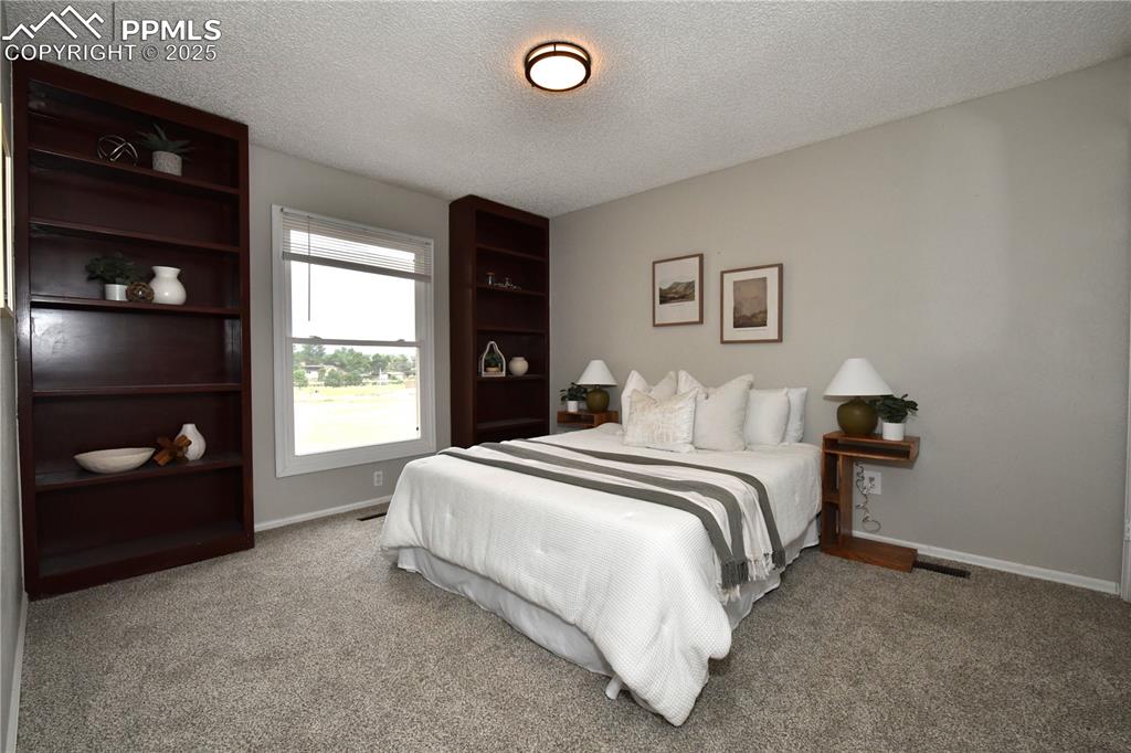 Image 16 of 36: Carpeted bedroom with a textured ceiling and baseboards
