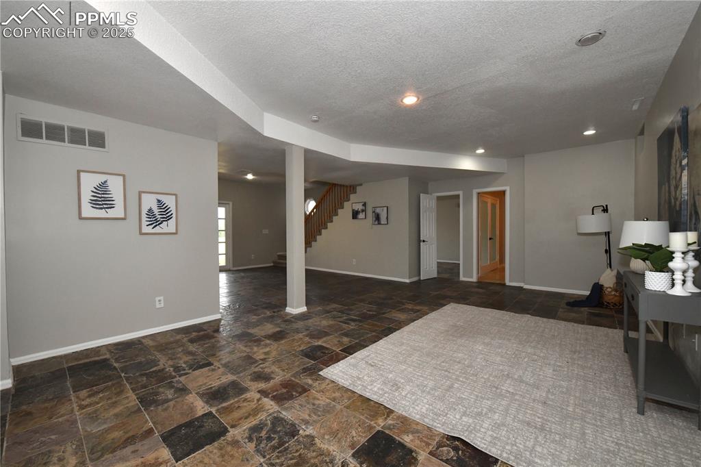 Image 25 of 36: Below grade area with stone finish floors, stairway, and a textured ceiling