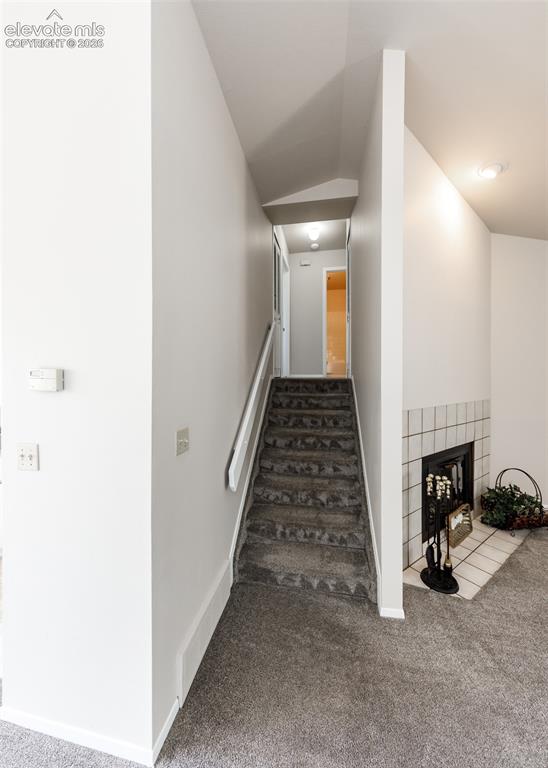 Image 19 of 36: Carpeted staircase with white handrail, recessed lighting, and a tiled fire