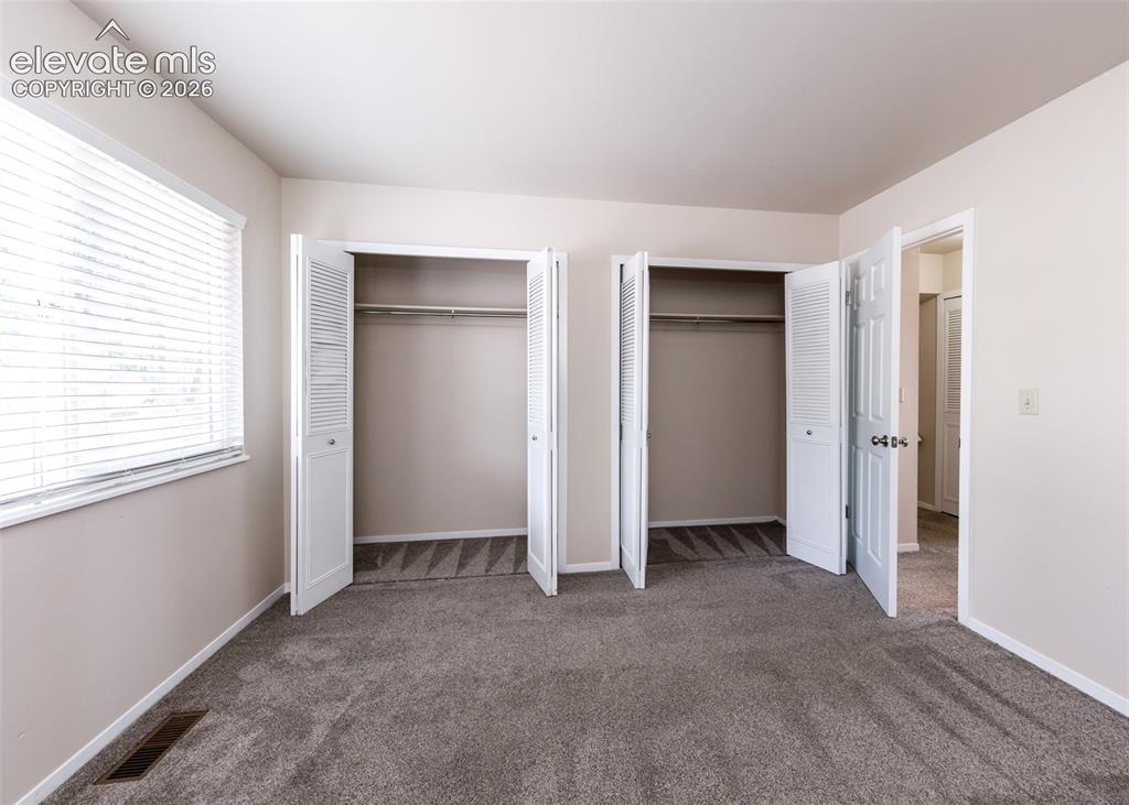 Image 25 of 36: Plush gray carpeting, dual bi-fold closets, window with horizontal blinds, 