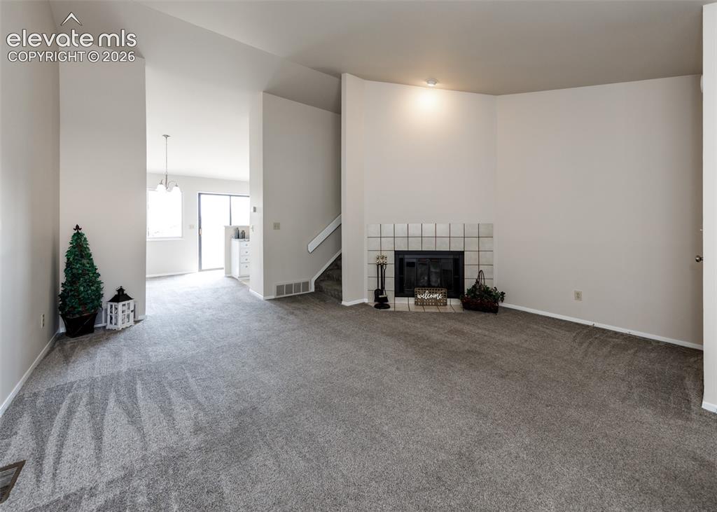 Image 8 of 36: Recessed lighting, tiled fireplace surround, carpeted flooring, staircase, 