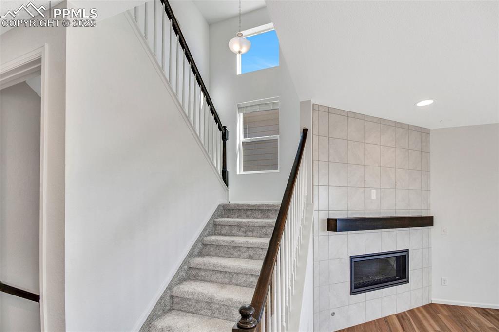 Image 14 of 46: Stairs featuring a fireplace, wood finished floors, and a towering ceiling