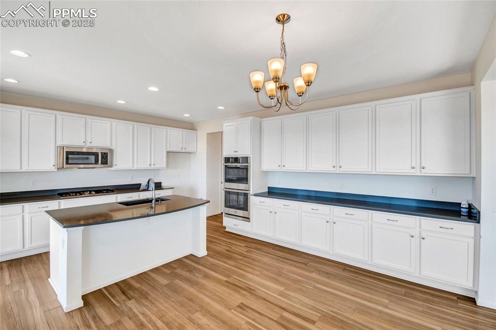Image 17 of 46: Kitchen with white cabinetry, hanging light fixtures, light wood-type floor