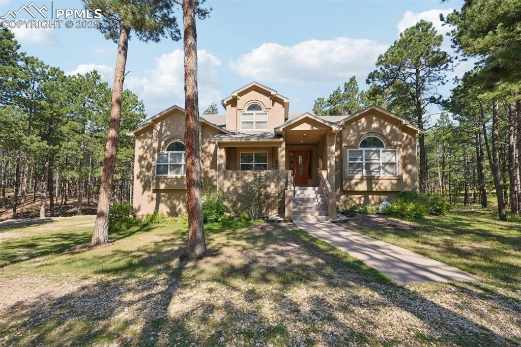 Caption: View of front facade with stucco siding and a front lawn