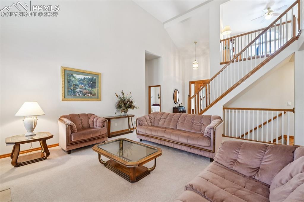 Image 12 of 45: Carpeted living room with a towering ceiling, stairs, and ceiling fan
