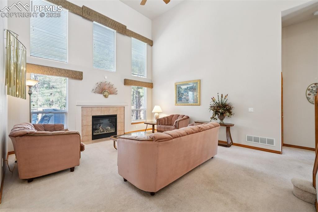 Image 13 of 45: Living room featuring a high ceiling, light colored carpet, a tile fireplac