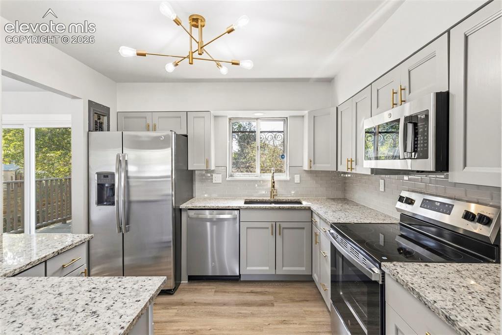 Image 16 of 46: Kitchen featuring gray cabinetry with gold hardware, granite countertops, s