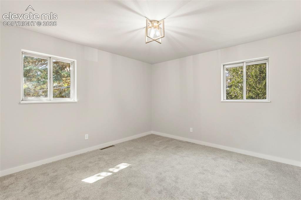 Image 21 of 46: Spacious room featuring light gray walls, plush carpeting, two windows, and