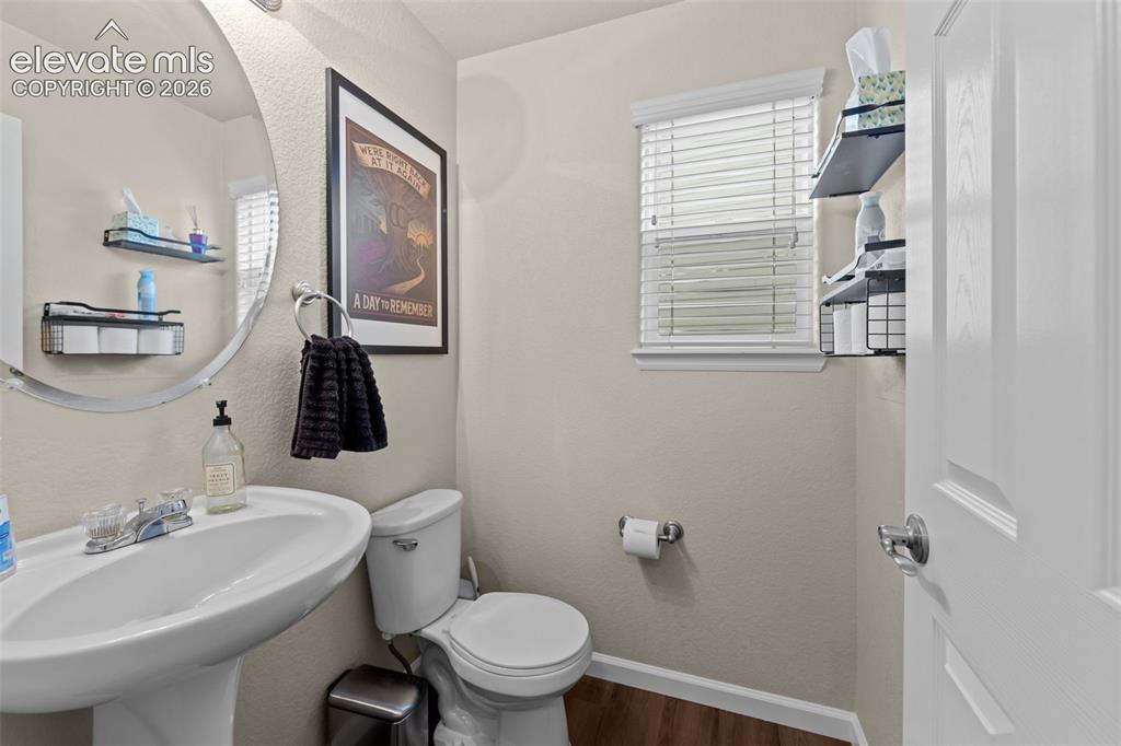 Image 11 of 41: Pedestal sink with chrome faucet, circular wall mirror, and wood-finish flo