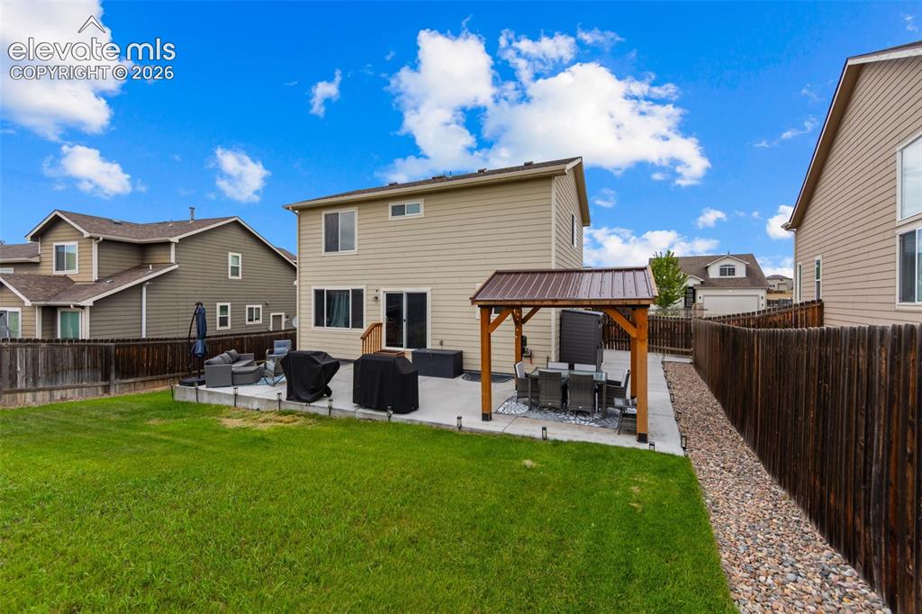 Image 29 of 41: Expansive backyard featuring a lush lawn, concrete patio, and a covered per