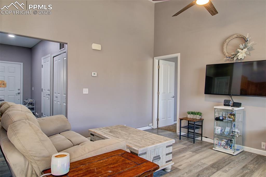 Image 14 of 21: Living room featuring ceiling fan, a high ceiling, and wood finished floors