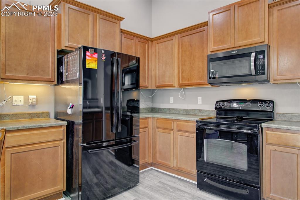 Image 15 of 21: Kitchen featuring black appliances, light countertops, and light wood finis