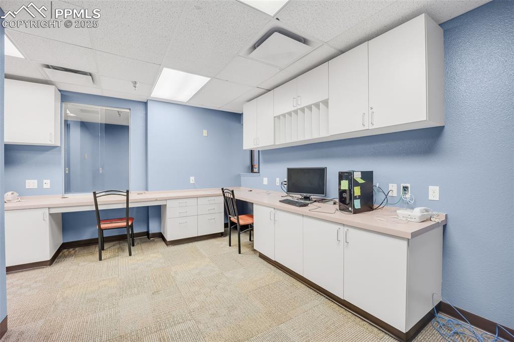 Image 28 of 49: Home office featuring built in study area, a paneled ceiling, and light col