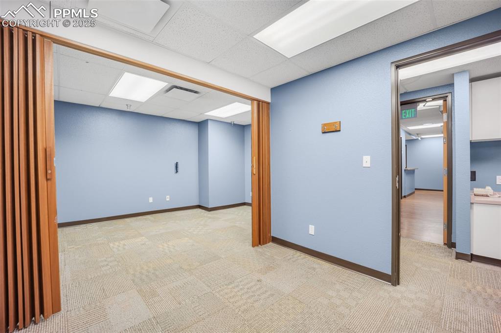 Image 29 of 49: Finished basement with light colored carpet and a paneled ceiling