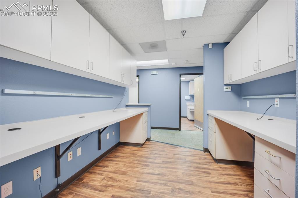 Image 33 of 49: Kitchen with light countertops, a drop ceiling, white cabinetry, light wood
