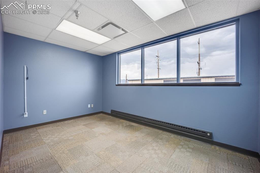 Image 41 of 49: Carpeted spare room with a baseboard radiator, a drop ceiling, and a penden