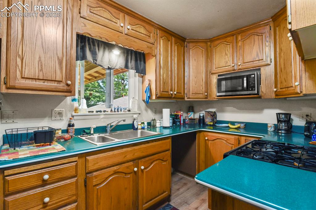 Image 10 of 30: Kitchen featuring stainless steel microwave, brown cabinetry, and wood fini