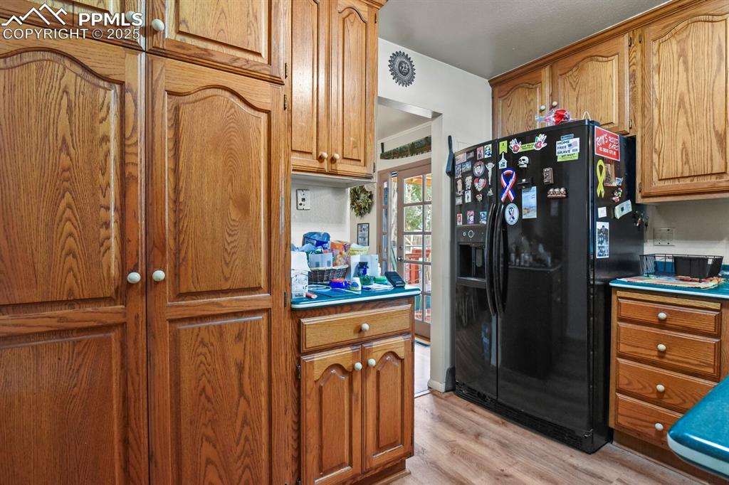 Image 11 of 30: Kitchen with black fridge, light wood finished floors, and brown cabinets
