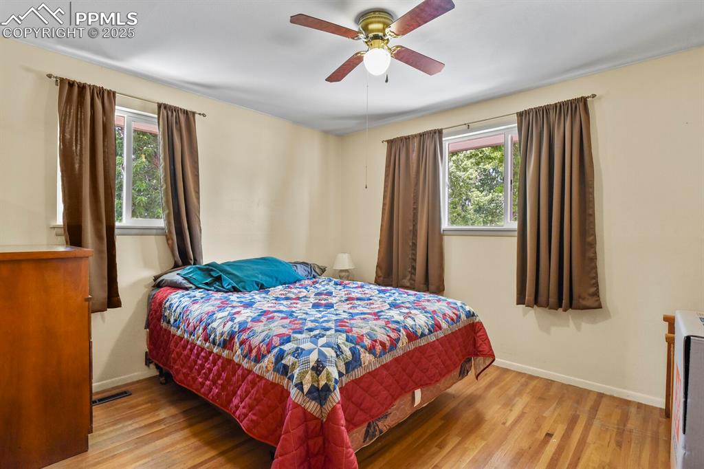 Image 16 of 30: Bedroom with wood finished floors, multiple windows, and ceiling fan