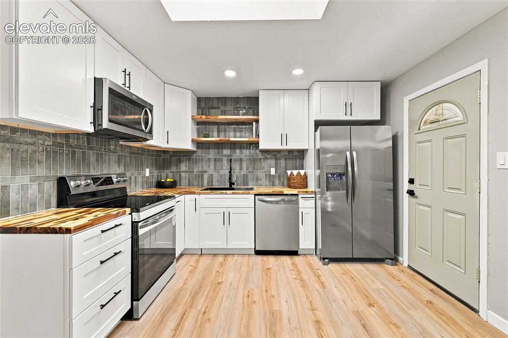 Image 10 of 30: Kitchen featuring light wood-finish flooring, white cabinetry with black ha
