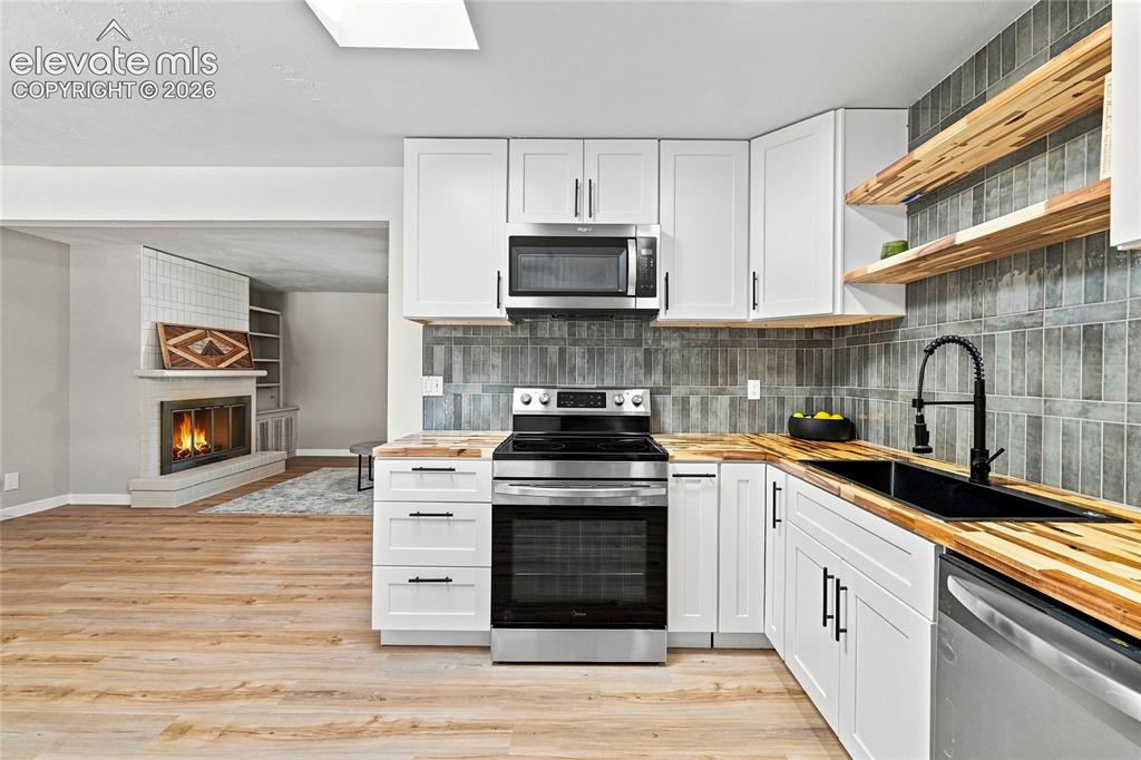 Image 11 of 30: Contemporary kitchen featuring white cabinetry, wood-finish countertops, st