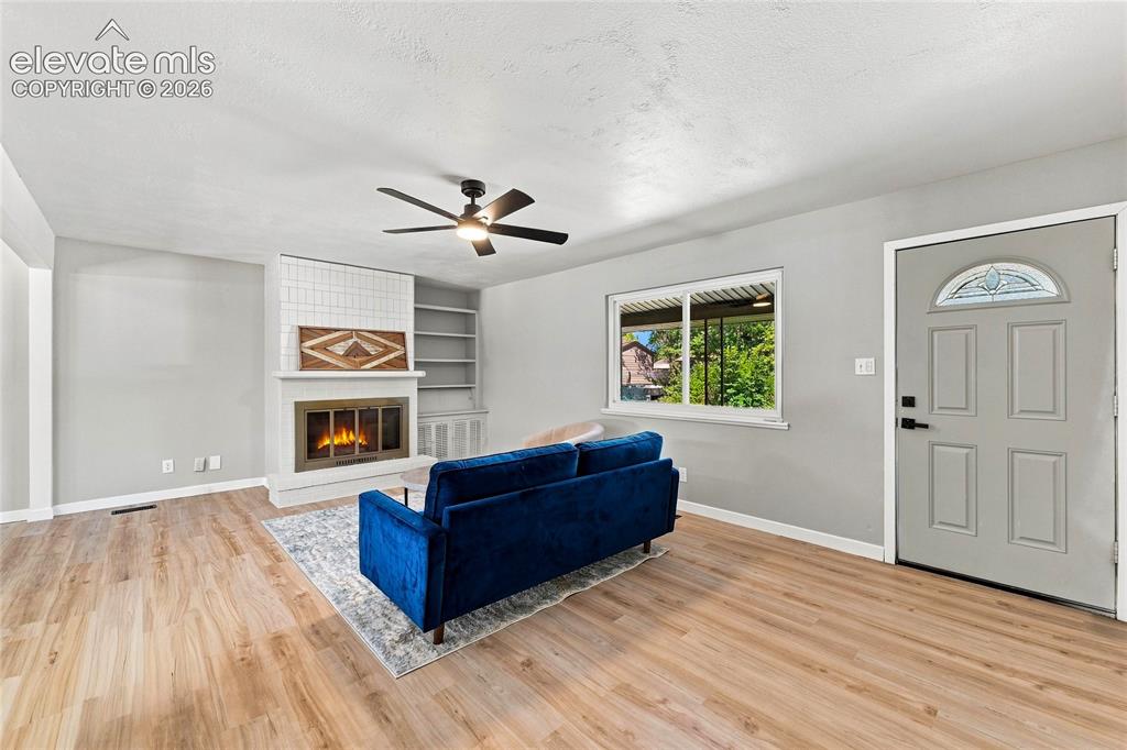 Image 3 of 30: Living area featuring wood-finish flooring, a ceiling fan, a fireplace with