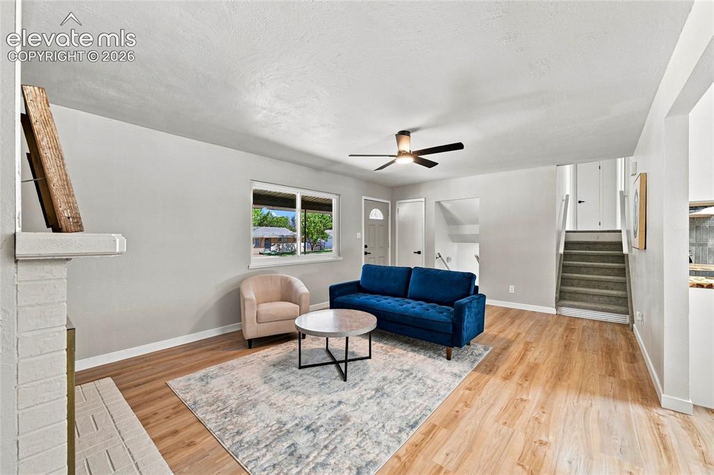 Image 5 of 30: Living area featuring wood-finish flooring, a white brick fireplace, a wind