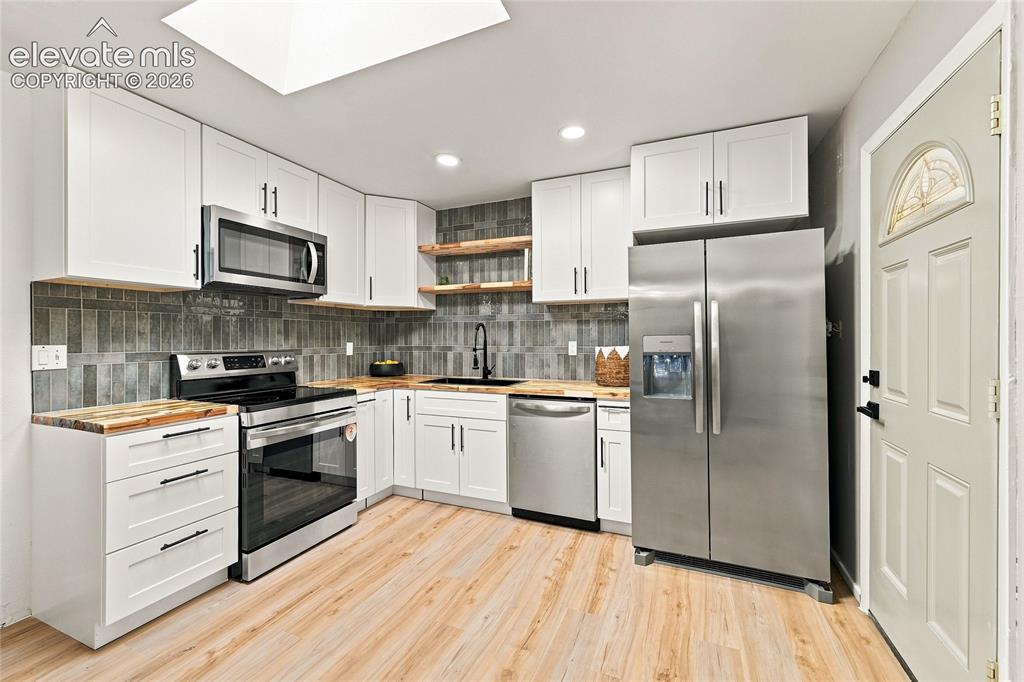 Image 9 of 30: White cabinetry, wood-finish countertops, stainless steel appliances, and a
