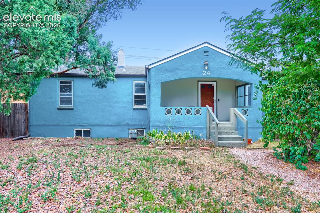 Caption: Stucco exterior, covered front porch, concrete steps, wood fencing, and mature trees