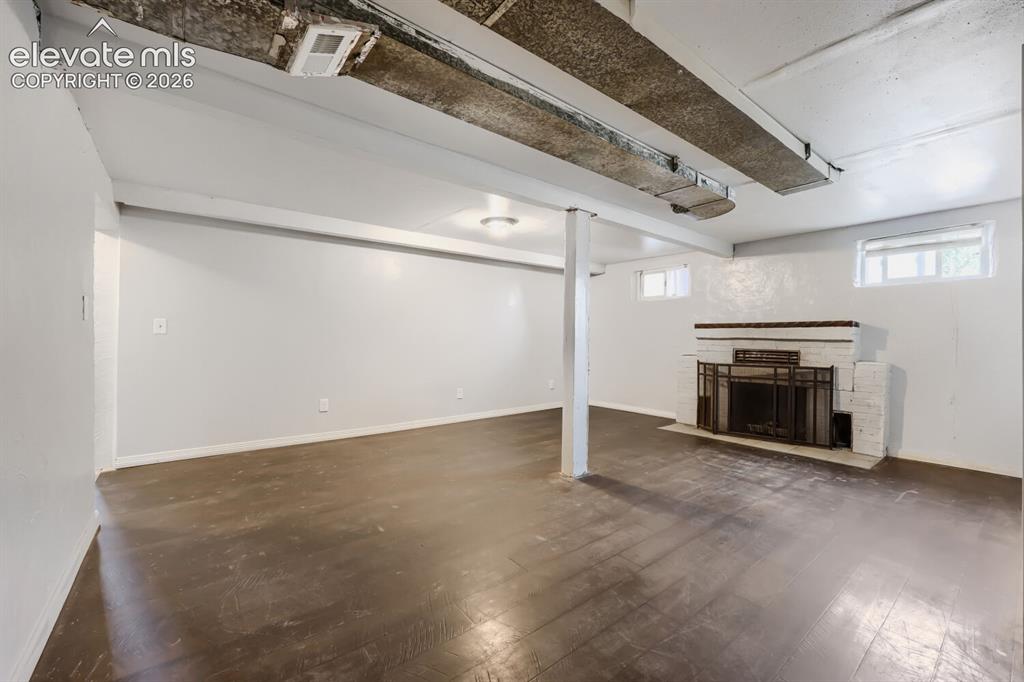 Image 18 of 36: Spacious room with dark wood-finish flooring, a white brick fireplace, and