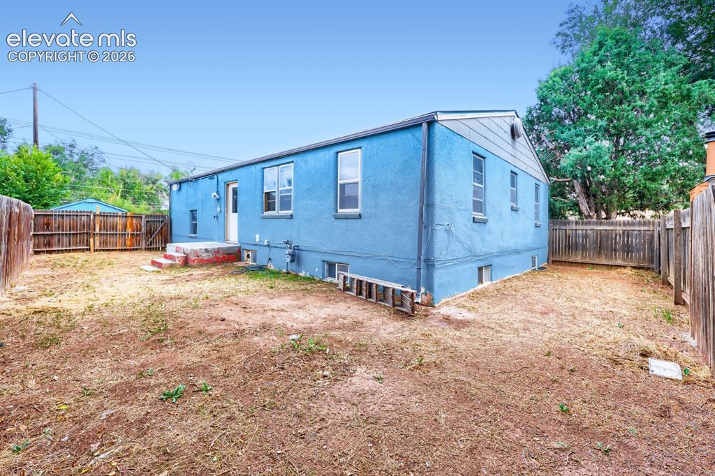 Image 34 of 36: Blue stucco exterior with multiple windows and a wood fence