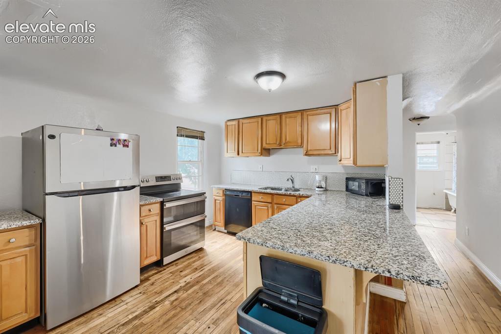 Image 7 of 36: Kitchen featuring stainless steel appliances, wood-finish flooring, light w