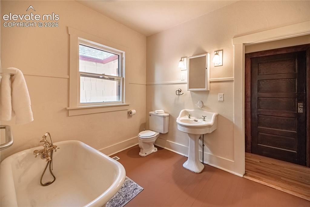 Image 14 of 47: Pedestal sink, clawfoot tub with brass fixtures, wood-paneled door, and a w