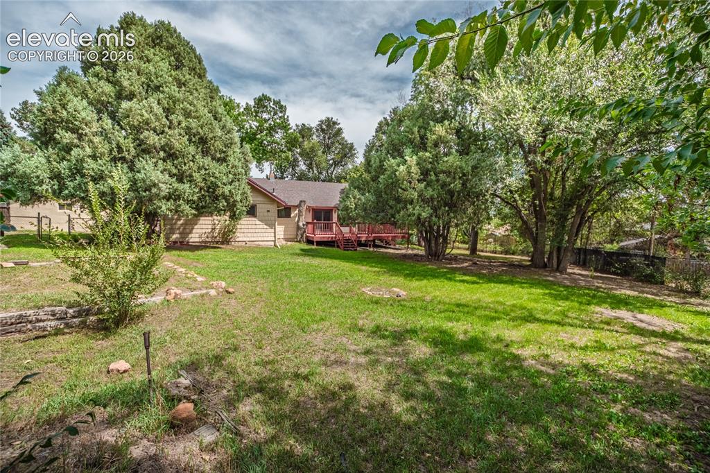 Image 41 of 47: Expansive grassy yard with mature trees and a multi-level wood deck