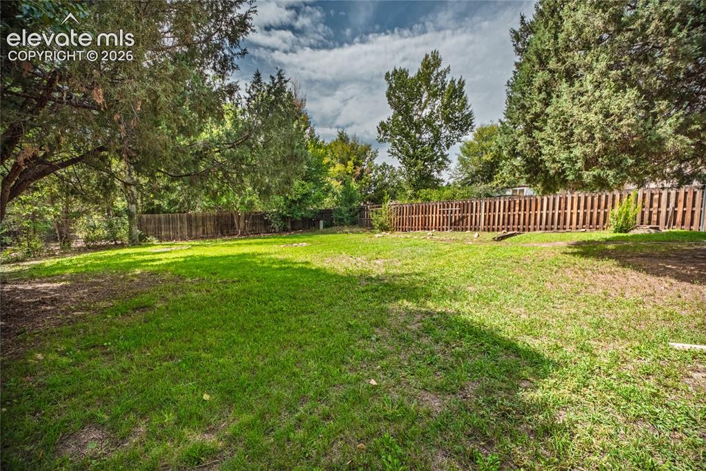 Image 42 of 47: Expansive grassy yard with mature trees and a wood privacy fence