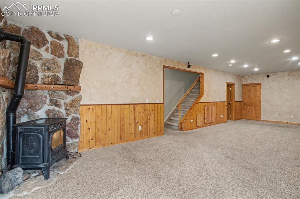 Image 22 of 49: Below grade area with a wood stove, wainscoting, carpet floors, wood walls,