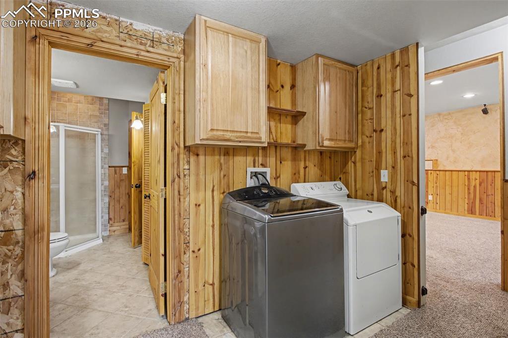 Image 27 of 49: Laundry area featuring wooden walls, a wainscoted wall, cabinet space, and