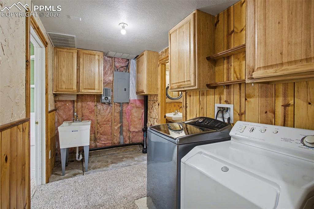 Image 28 of 49: Laundry area featuring wood walls, a textured ceiling, concrete flooring, e