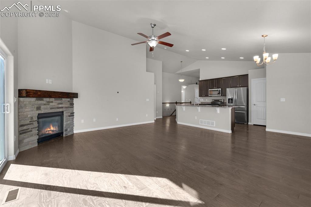 Image 5 of 38: Living area with cozy fireplace, ceiling fan, high vaulted ceiling, and woo
