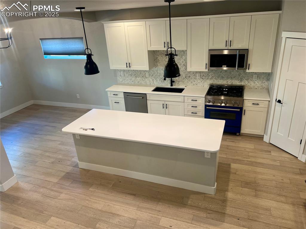 Image 11 of 19: Kitchen with stainless steel appliances, white cabinetry, and hanging light