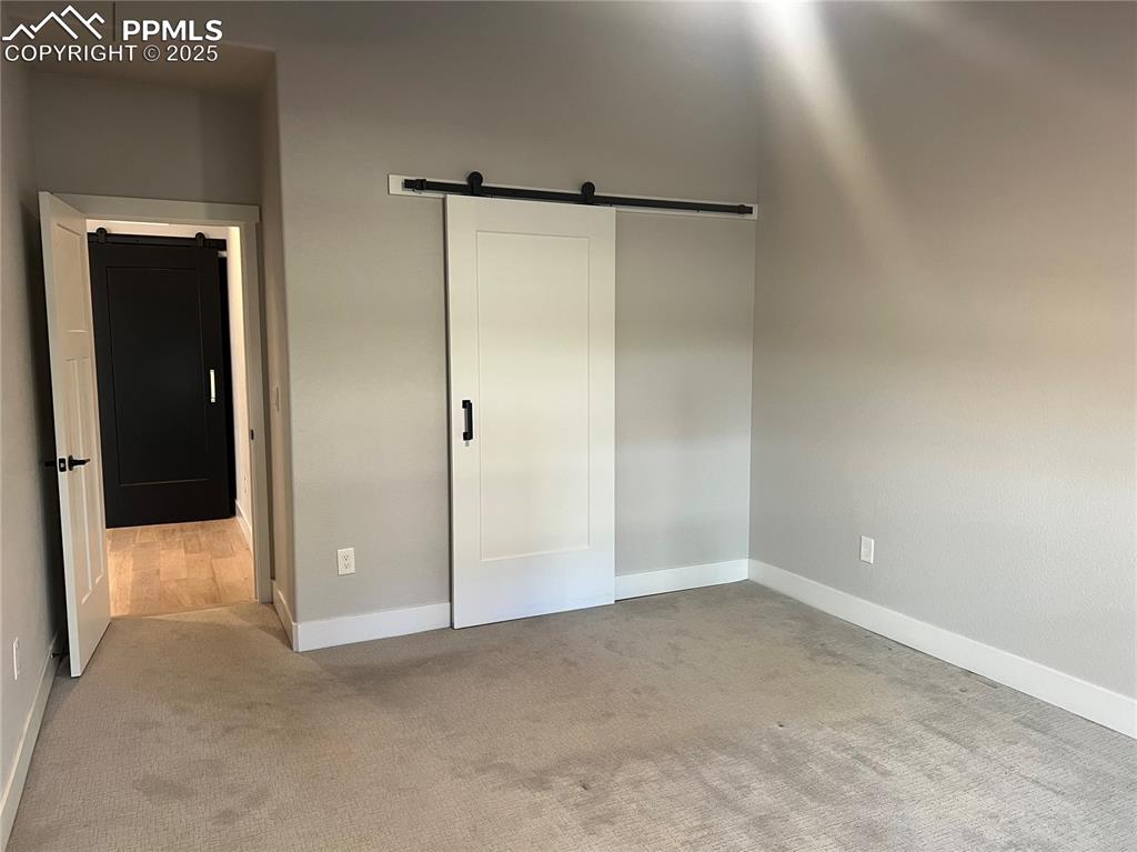 Image 6 of 19: Unfurnished master bedroom featuring a barn door and light colored carpet
