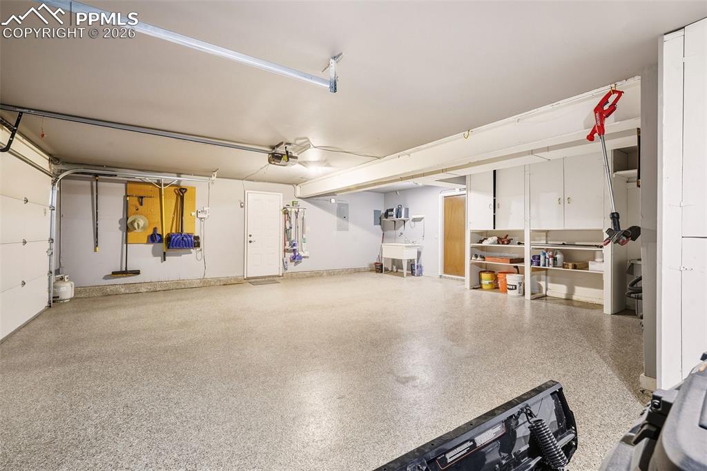 Image 37 of 50: Oversized garage with epoxy-coated flooring, built-in shelving, utility sin