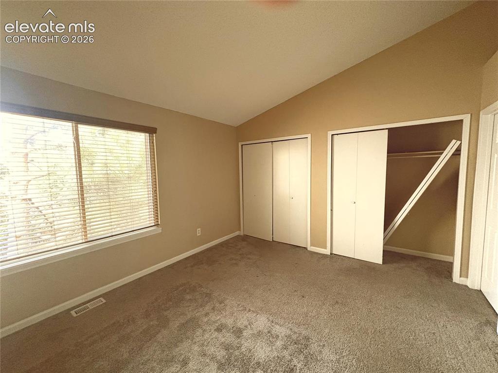 Image 18 of 31: The vaulted Primary Bedroom has neutral carpet, double closets, and an adjo