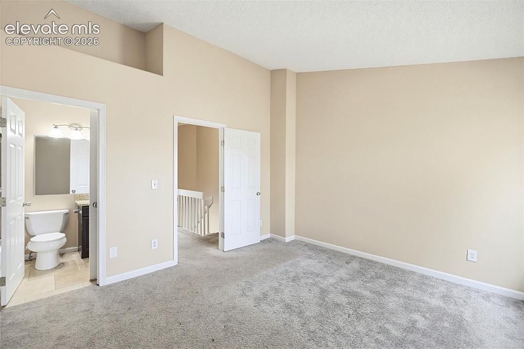 Image 21 of 31: The vaulted Primary Bedroom has neutral carpet, double closets, and an adjo
