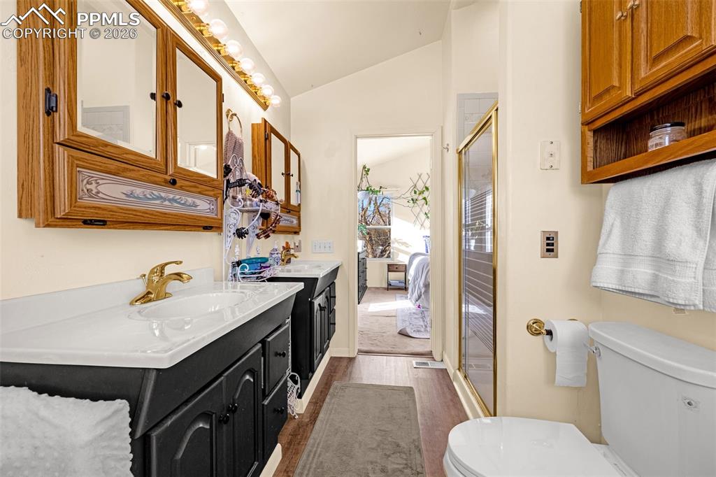 Image 23 of 38: Full bathroom featuring vaulted ceiling, two vanities, a stall shower, dark