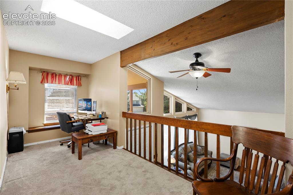 Image 13 of 43: Carpeted loft area featuring a skylight, a wood beam, a ceiling fan, and a 