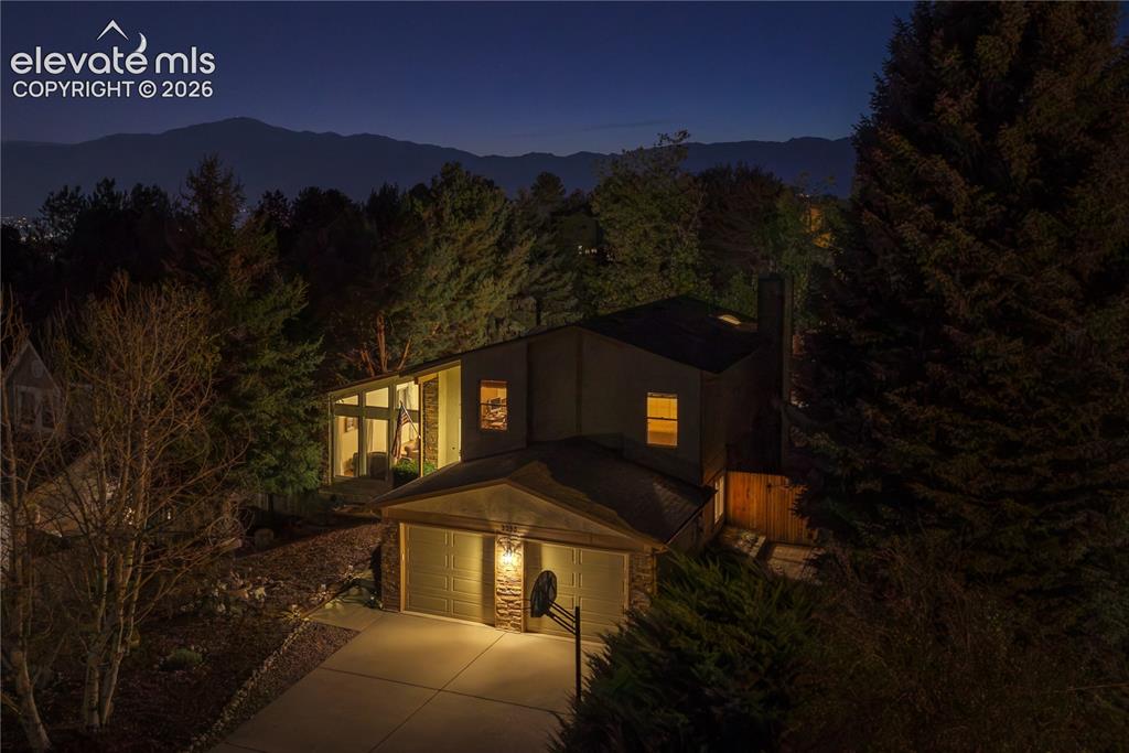 Image 2 of 43: Two-car garage, exterior stone accents, prominent chimney, mature trees, an