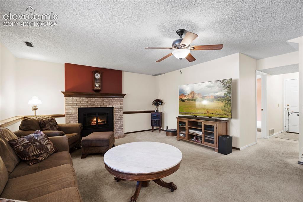 Image 20 of 43: Living room featuring a brick fireplace with a wood mantle, ceiling fan wit