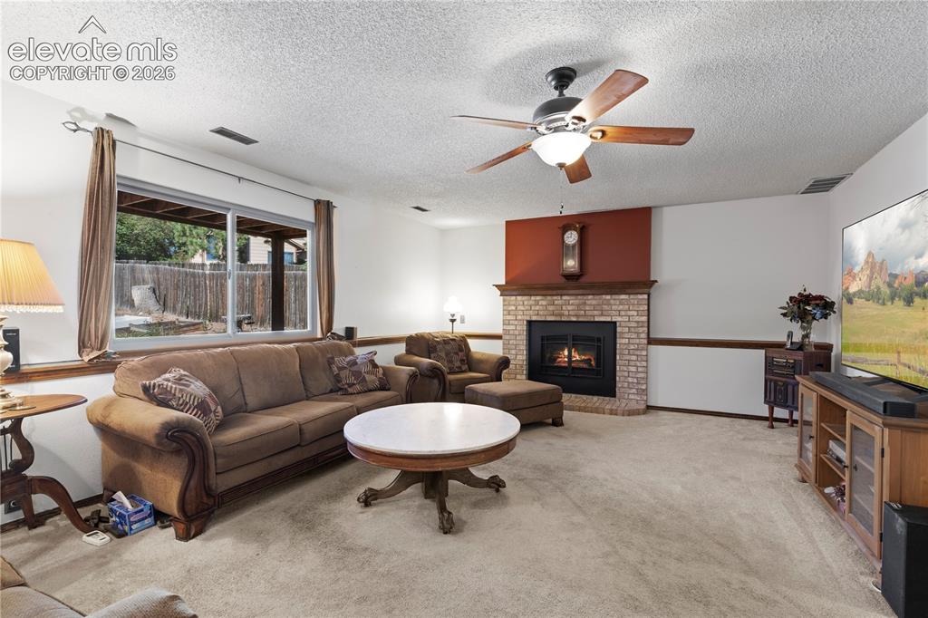 Image 21 of 43: Carpeted living area featuring a brick fireplace with a wood mantle, ceilin